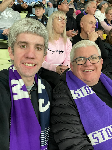 Dad and I at the Storm vs Sharks wearing purple Melbourne Storm scarfs. 
Jeremy is wearing a newer style storm scarf and has a smile. Jonathan is wearing a more traditional two colour stripe storm scarf and has a massive smile. 